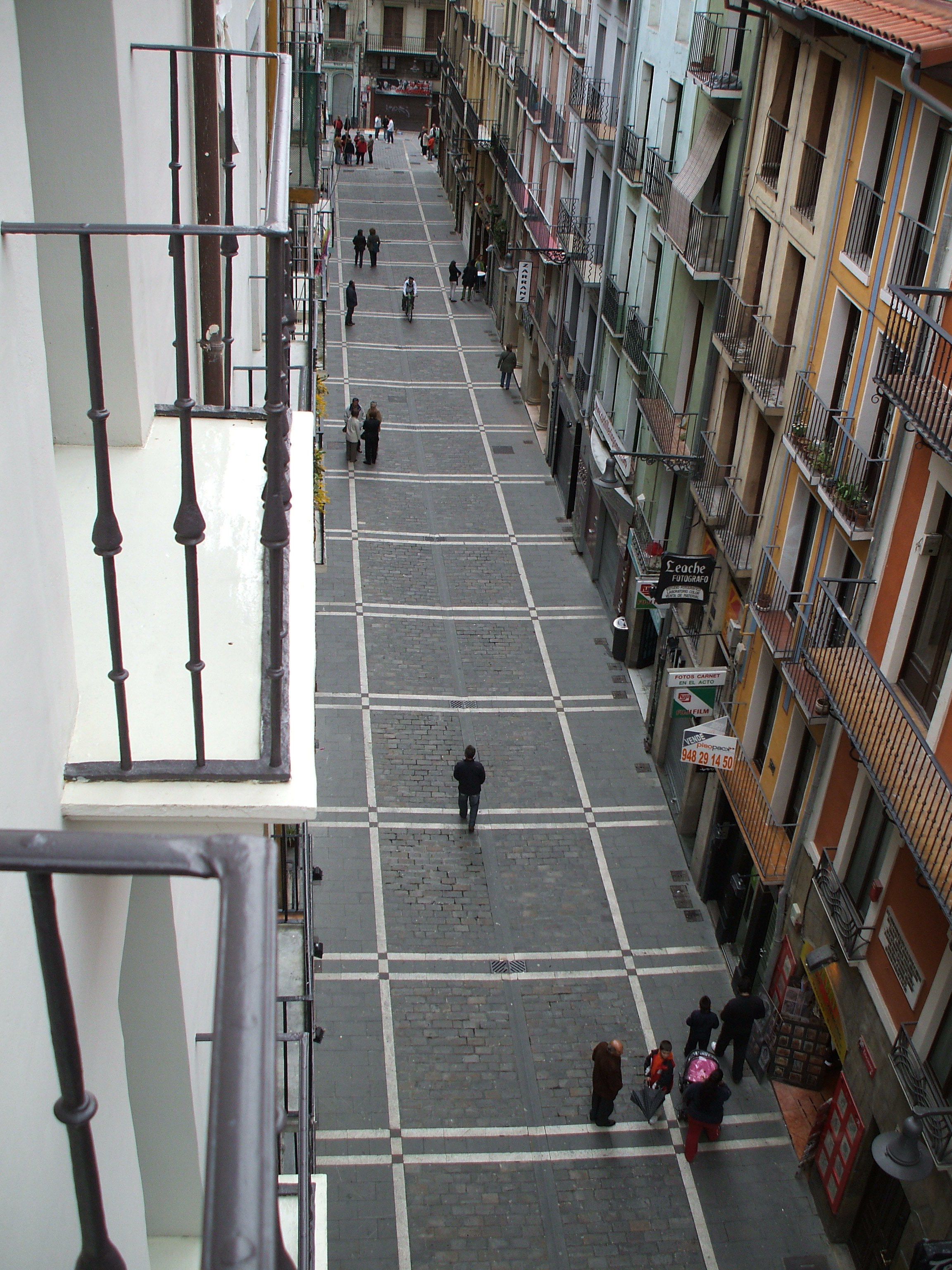Una vista di strada con edifici su entrambi i lati, un attraversamento pedonale e alcune persone che camminano.