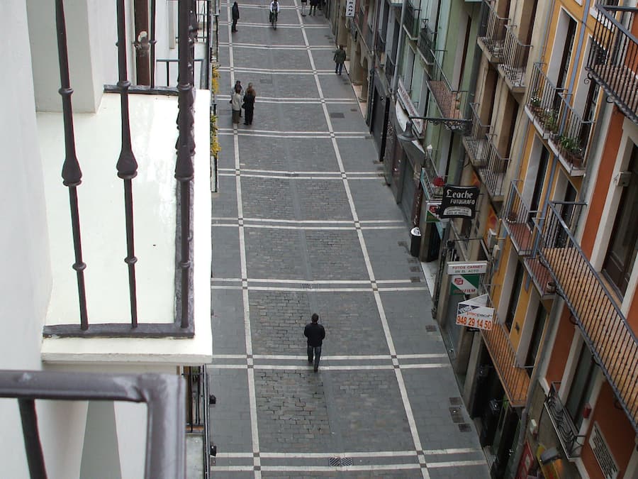 A street view with buildings on both sides, a pedestrian crossing, and a few people walking.