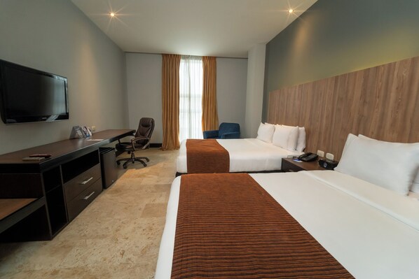 A hotel room with two beds, a desk, a chair, a TV, and a window with curtains.