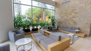 A modern lounge area with a large sectional sofa, armchairs, and a round coffee table. There are potted plants and a stone wall in the background.