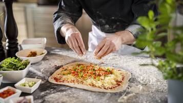 Eine Person bereitet Pizza an einem Tisch mit verschiedenen Zutaten und Schüsseln zu.