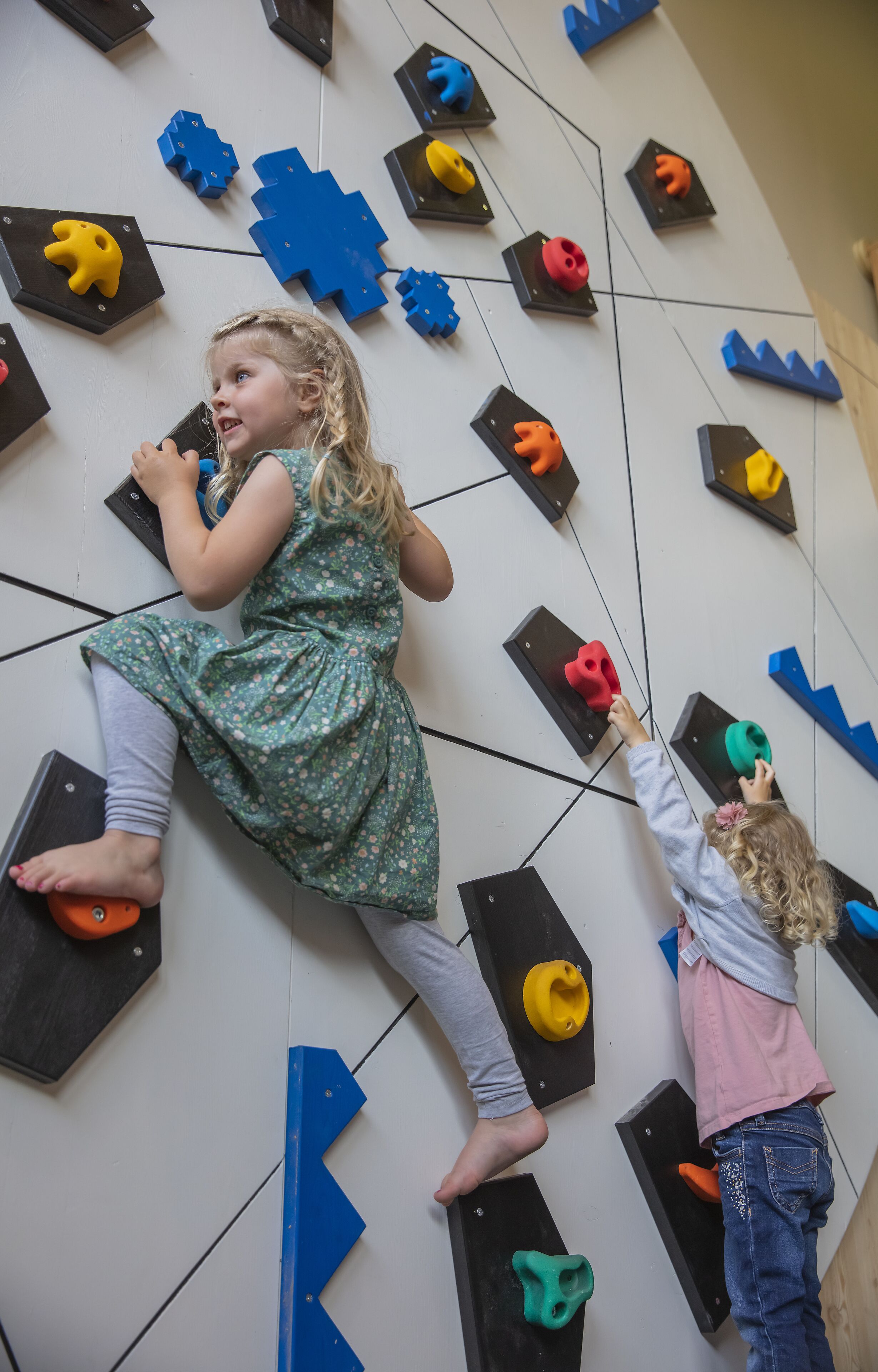Two children climbing a wall with variously shaped holds.