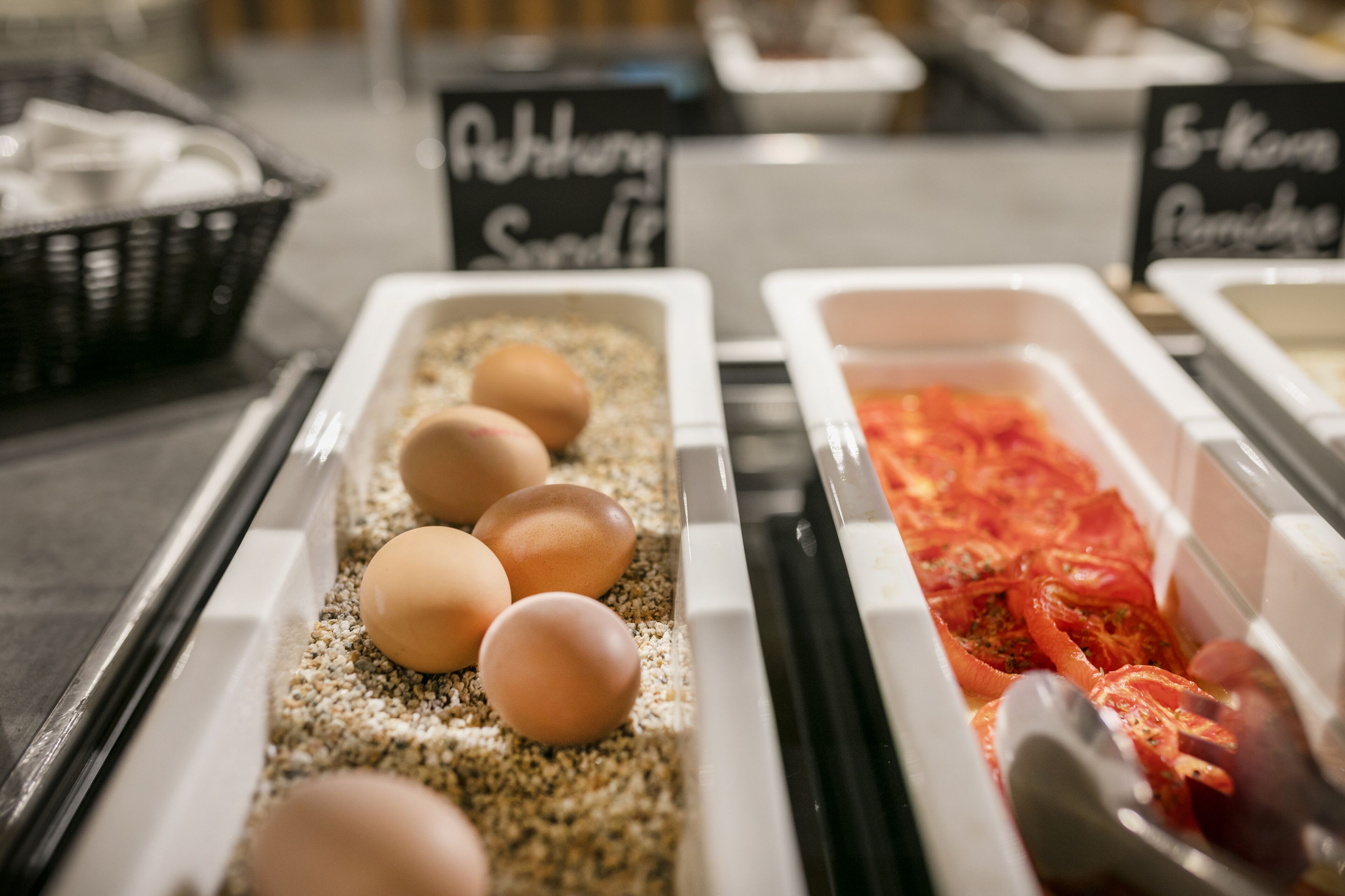 Un bufé de desayuno con recipientes etiquetados de huevos y tomates.