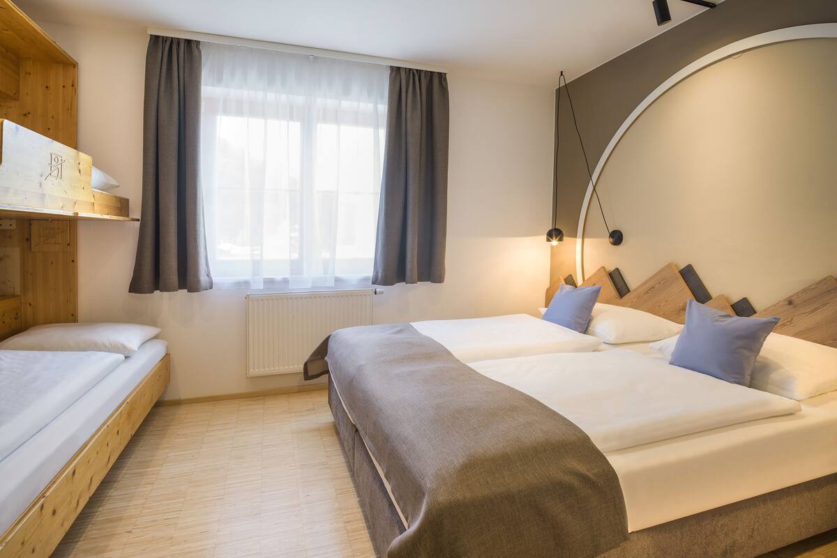A hotel room with a wooden bed, a window with curtains, a radiator, and a lamp.
