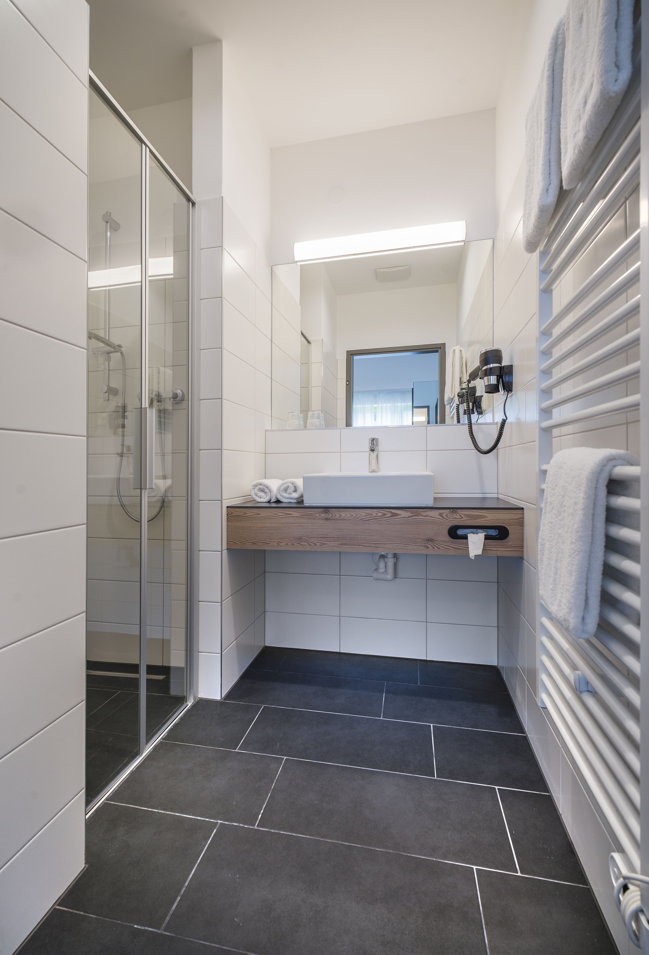 A modern bathroom with a glass shower enclosure, a wooden vanity, and a towel rack.