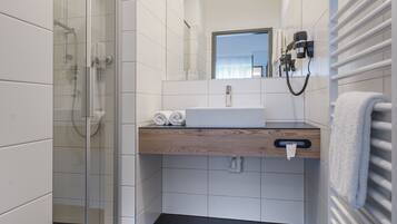 A modern bathroom with a glass shower enclosure, a wooden vanity, and a towel rack.