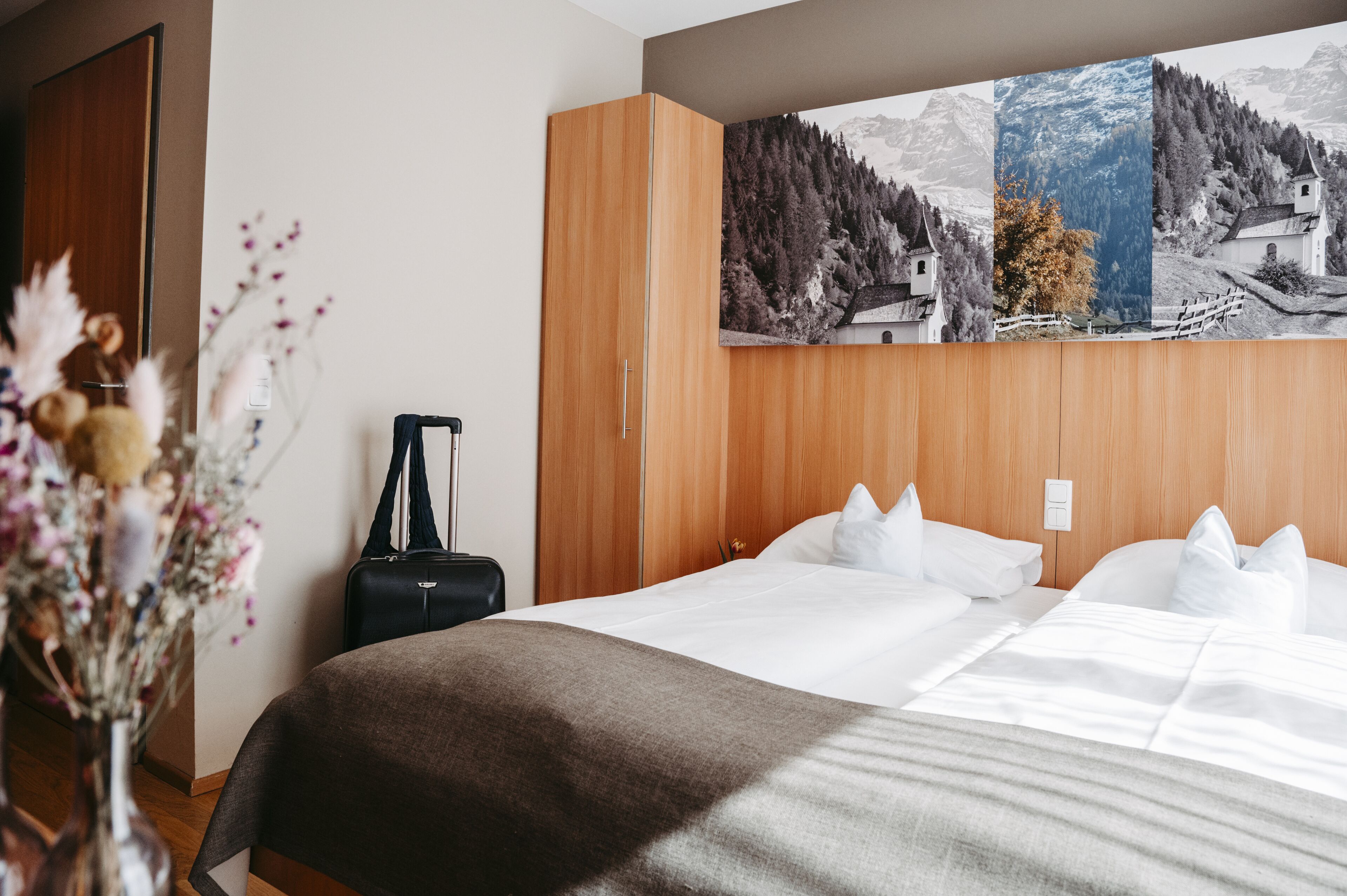 Una habitación de hotel con una cama grande, un armario de madera y un cuadro de un paisaje montañoso.