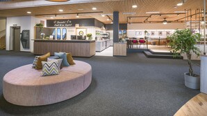 A spacious lobby with a central seating area, a reception desk, and a staircase leading to an upper level. - JUFA Hotel Wipptal (Steinach am Brenner)