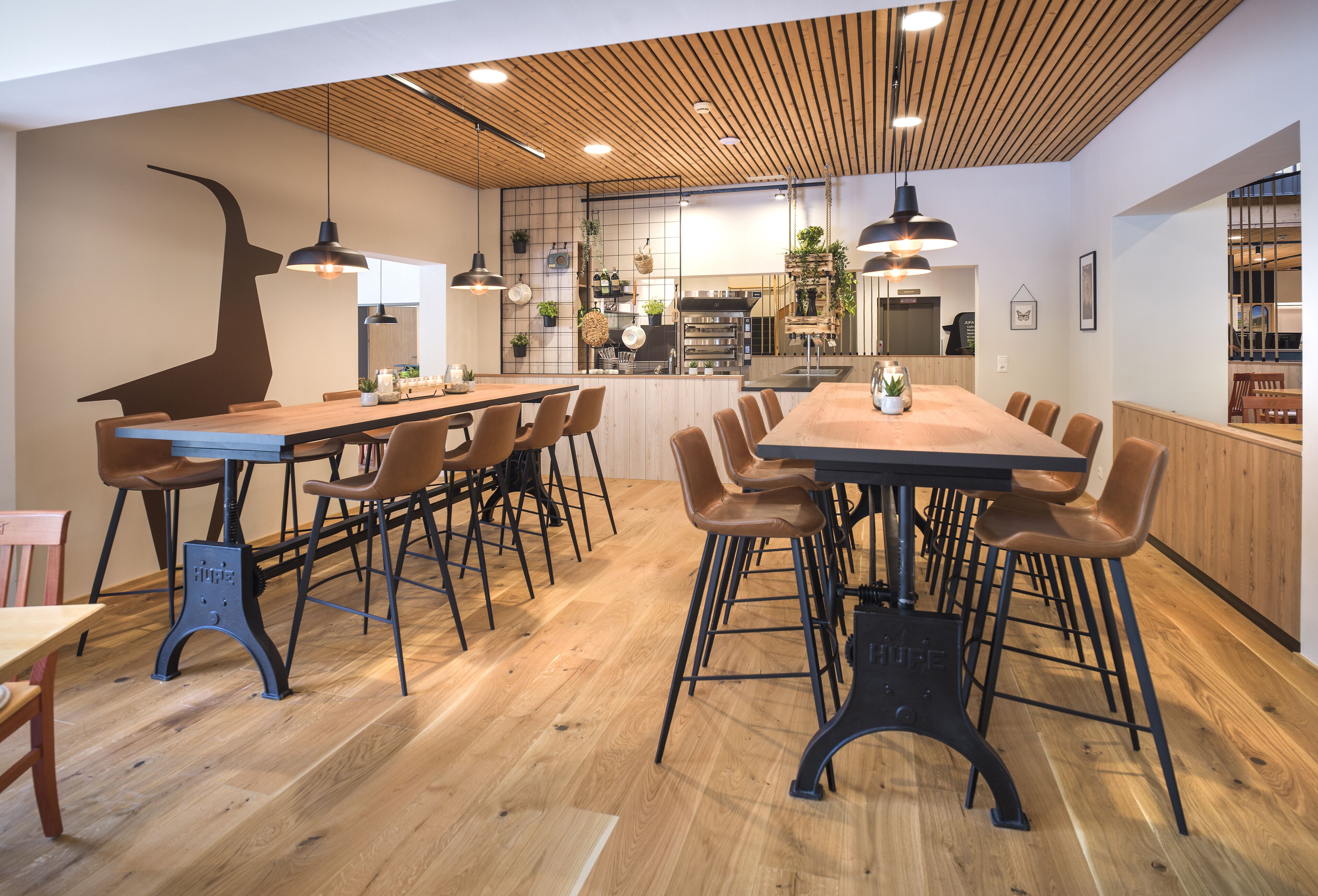 A modern restaurant with wooden flooring, a long communal table, and multiple chairs.