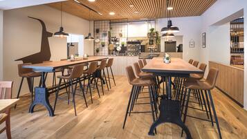 A modern restaurant with wooden flooring, a long communal table, and multiple chairs.