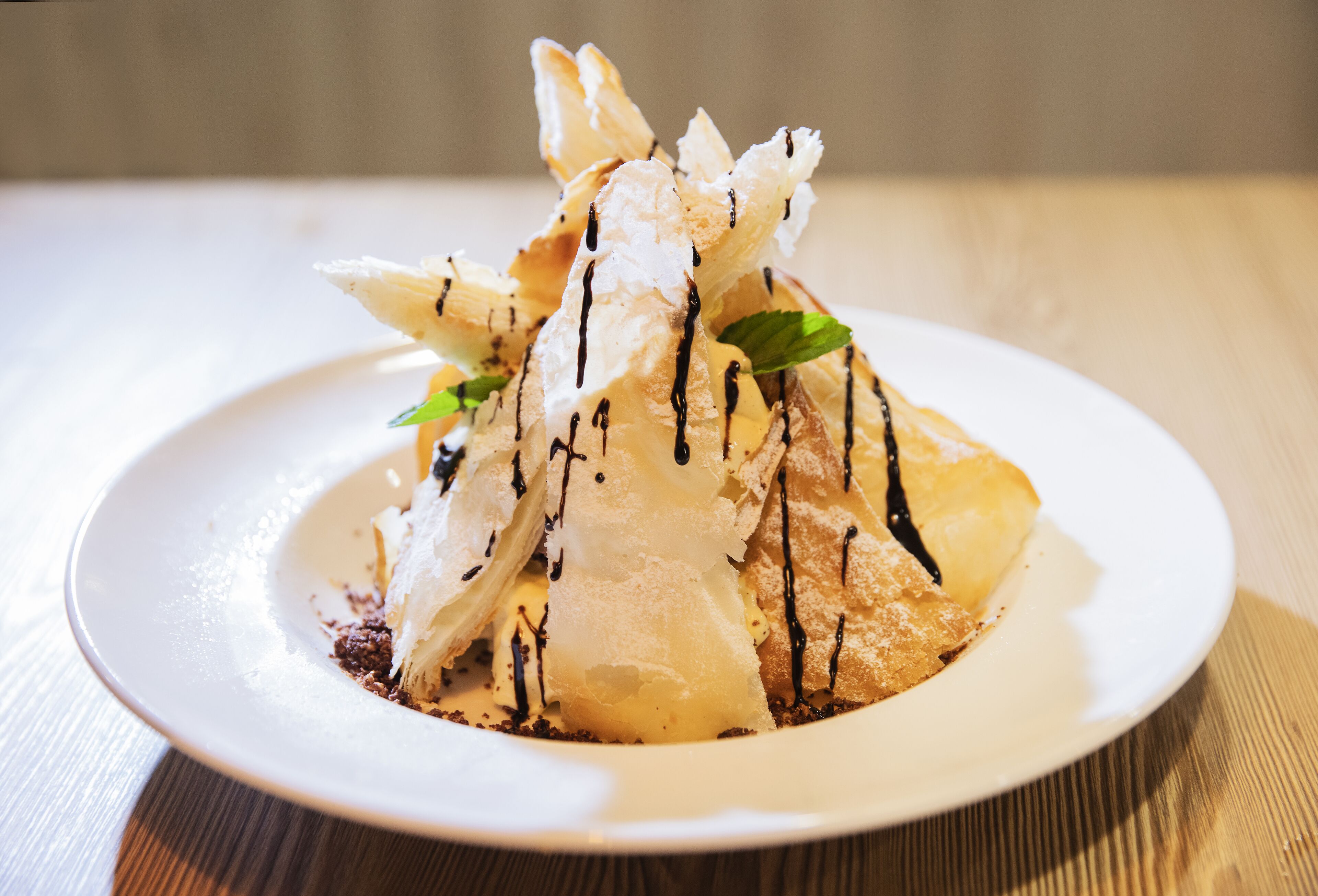 A dessert on a white plate with chocolate drizzle and mint leaves.
