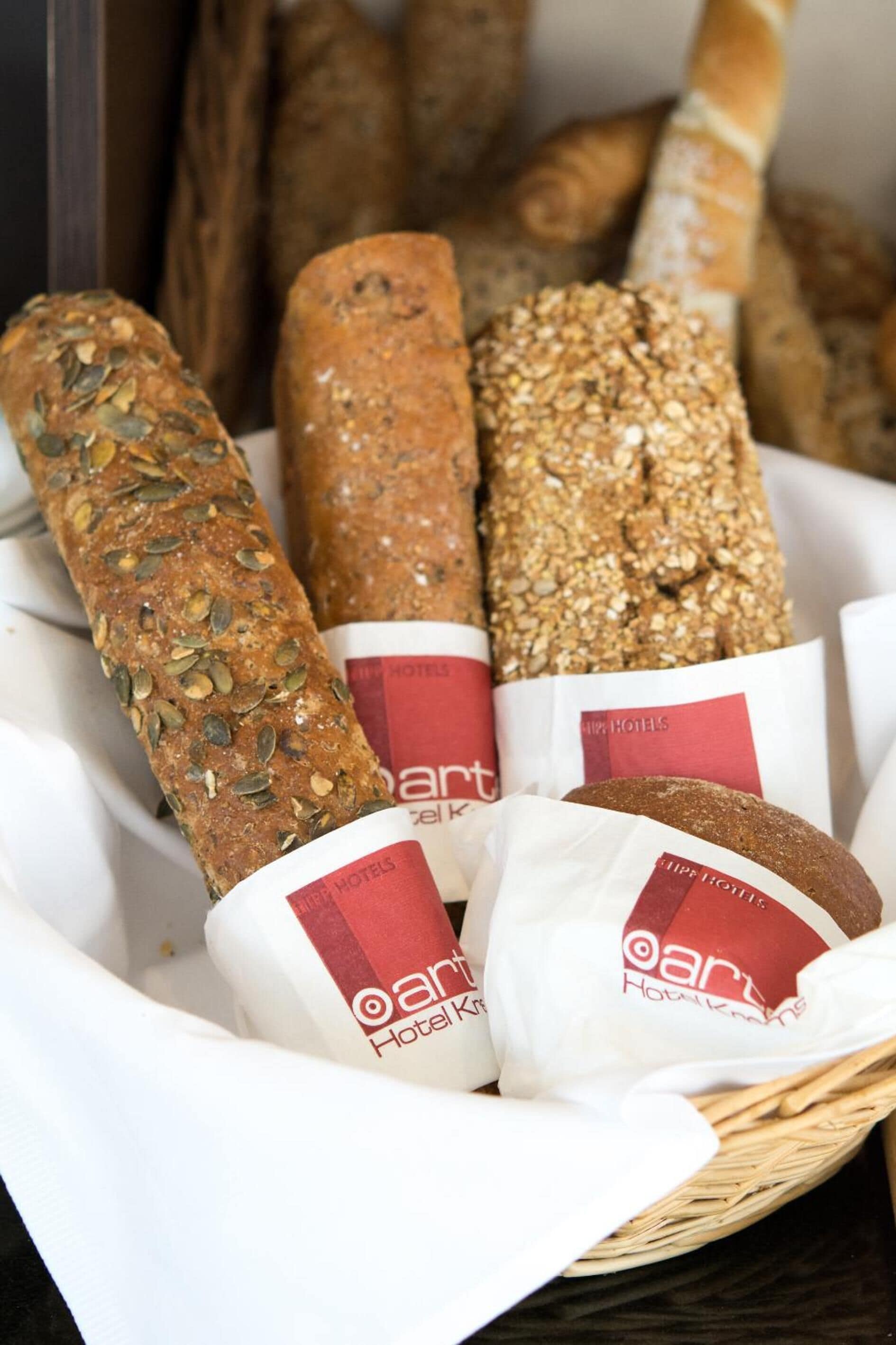 A basket containing various types of bread, some with labels indicating they are from a hotel bakery.