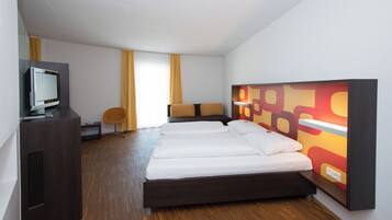 A modern hotel room with a bed, a desk with a computer, a chair, and a TV.