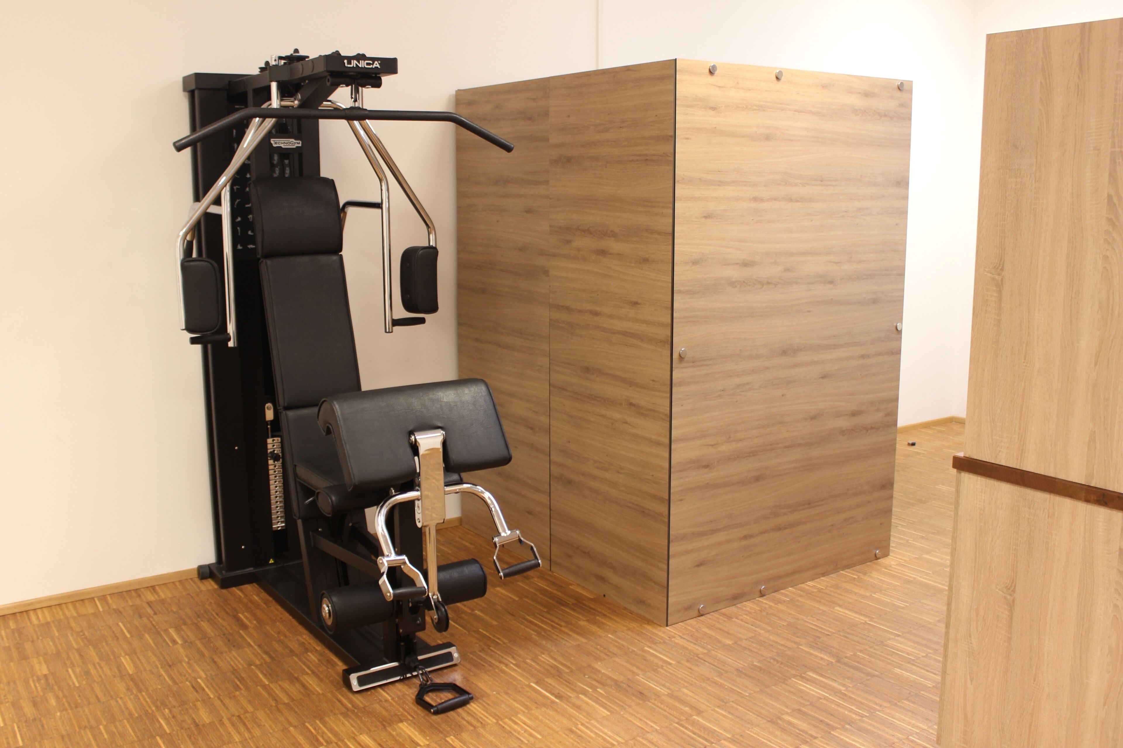 A gym with exercise equipment, a wooden cabinet, and a wooden floor.