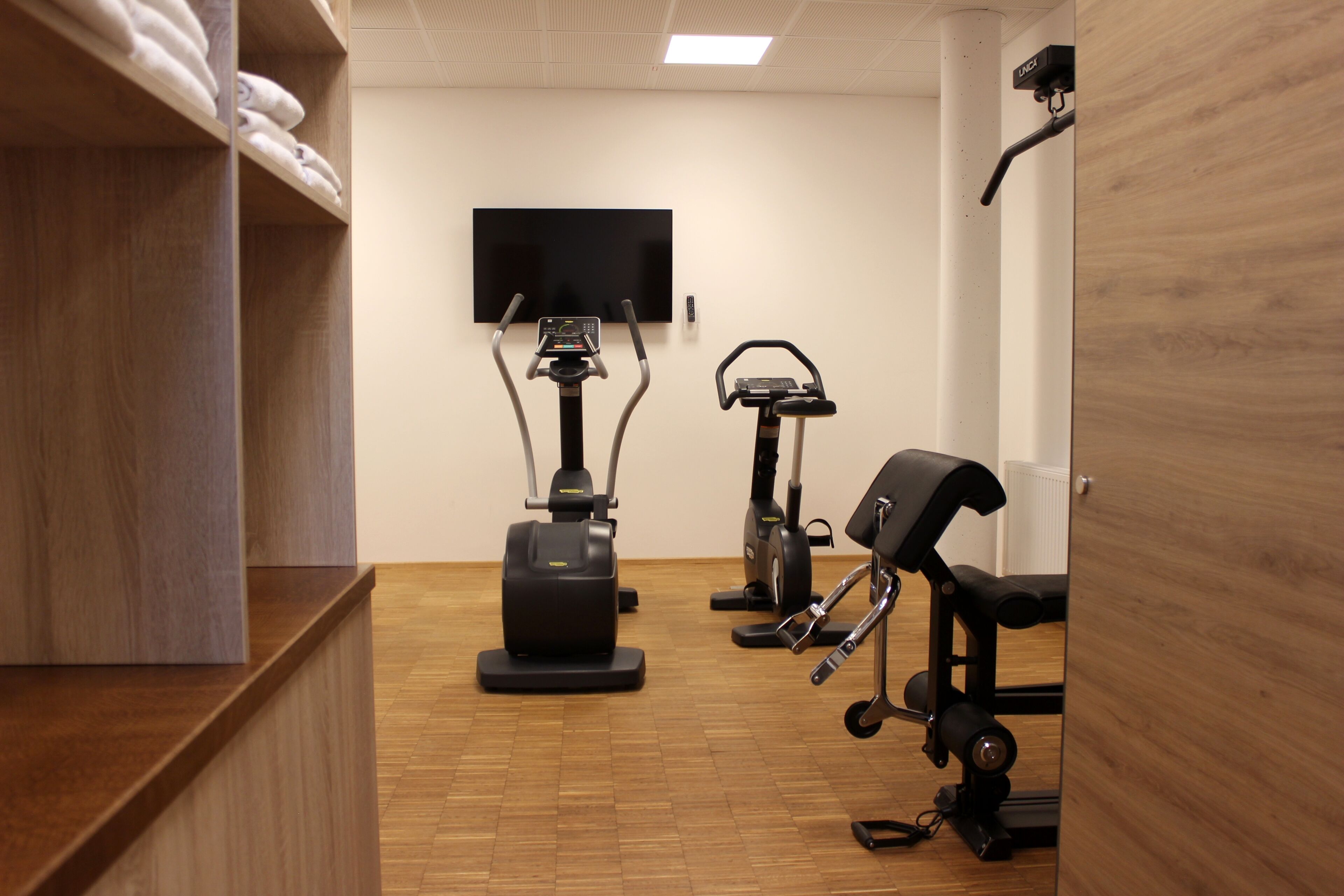 Ein Fitnessraum mit Trainingsgeräten, einem Fernseher und Holzboden.