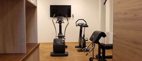 Un gimnasio con equipamiento de ejercicio, un televisor y piso de madera.