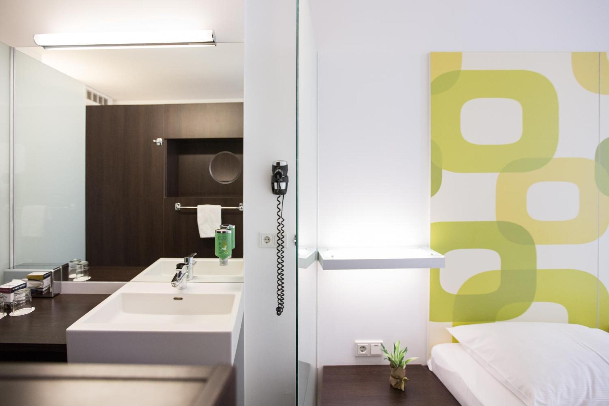 A modern bathroom with a large mirror, a white sink, and a towel hanging on the wall.