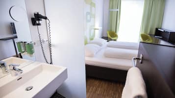 Quarto de hotel com banheiro, cama e escrivaninha.