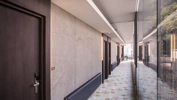 Un pasillo con piso estampado, una puerta con el número 127 y un muro de cristal que refleja el exterior.