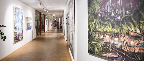 A hallway with art installations on the walls, wooden flooring, and a cityscape painting on the right.