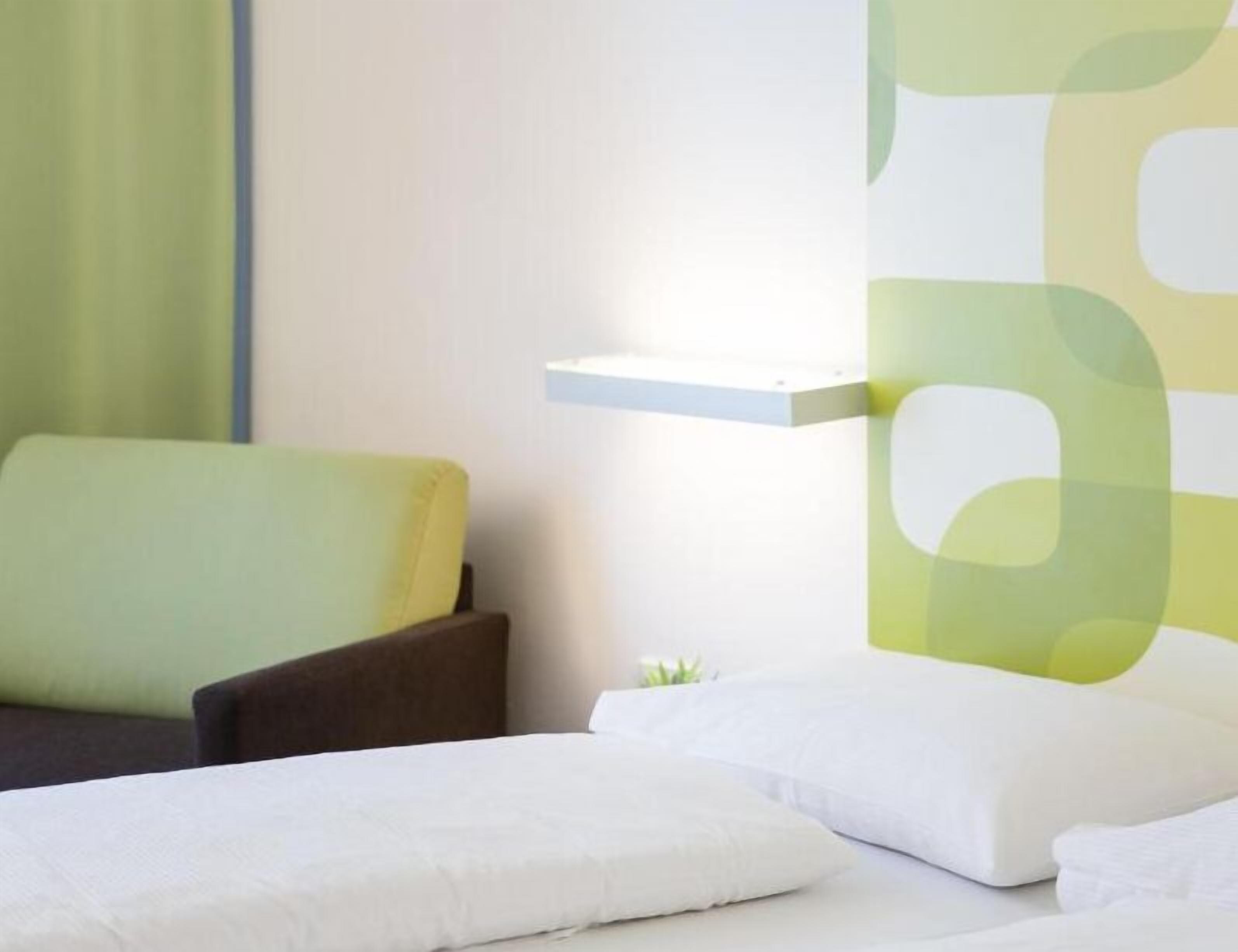 Una habitación de hotel con una cama, una silla y una mesita de noche con lámpara.