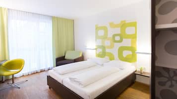 Habitación de hotel con cama, una silla, escritorio y un ventanal con cortinas.