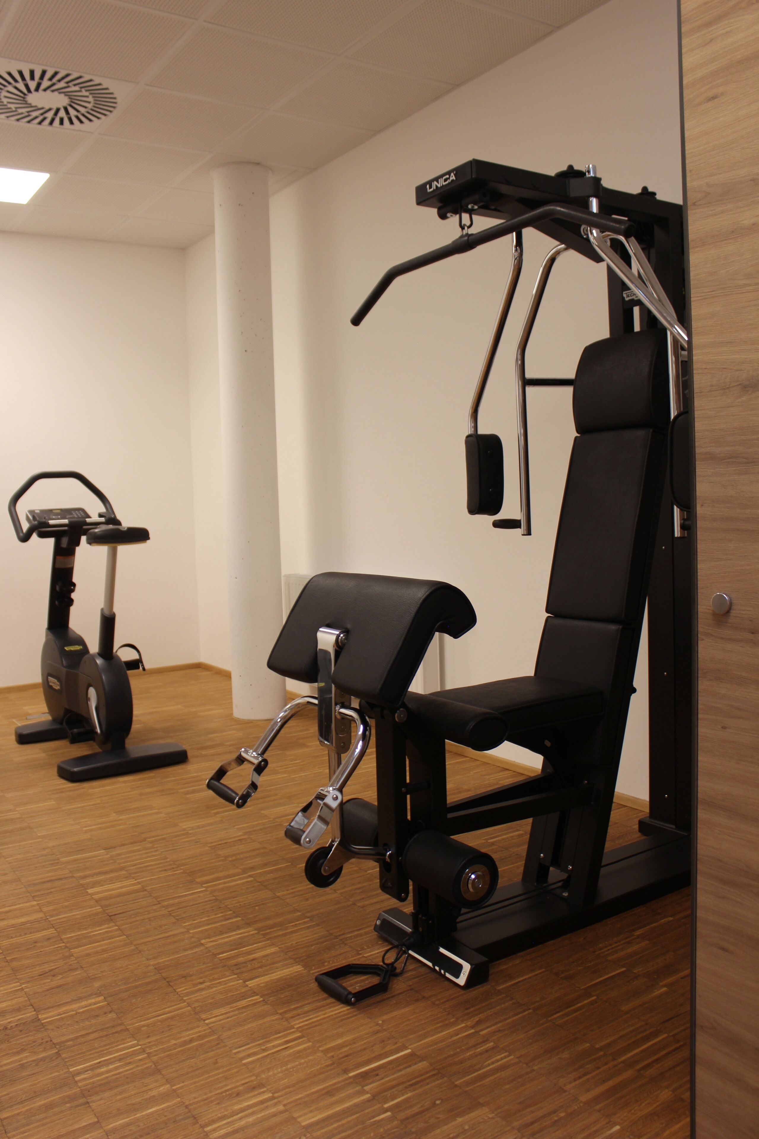 Un gimnasio con equipamiento de ejercicio, incluyendo una bicicleta estática, una máquina de pesas y una banca.