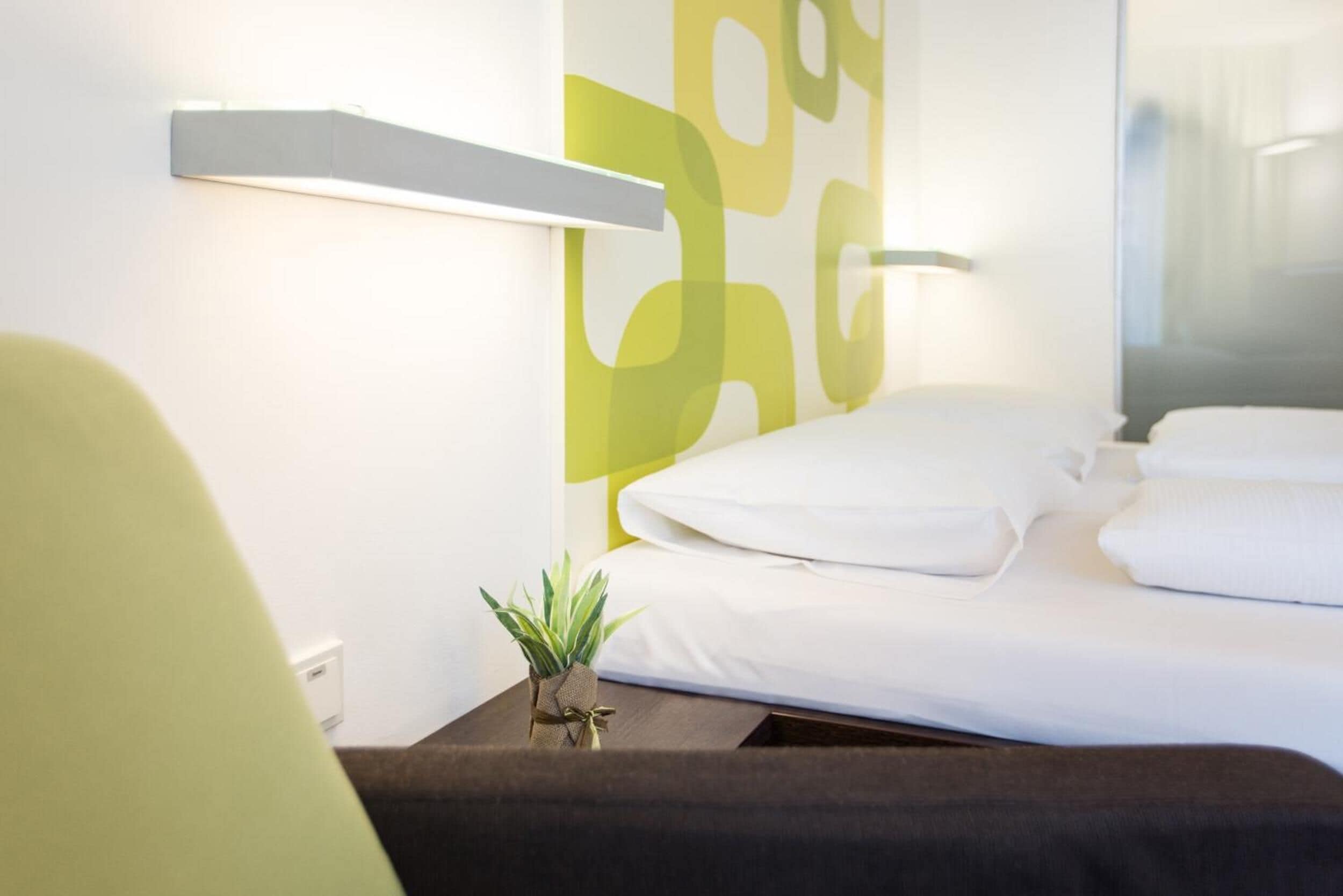 Une chambre d’hôtel avec un lit, une table de chevet ornée d’une plante et un mur décoré d’un motif géométrique.
