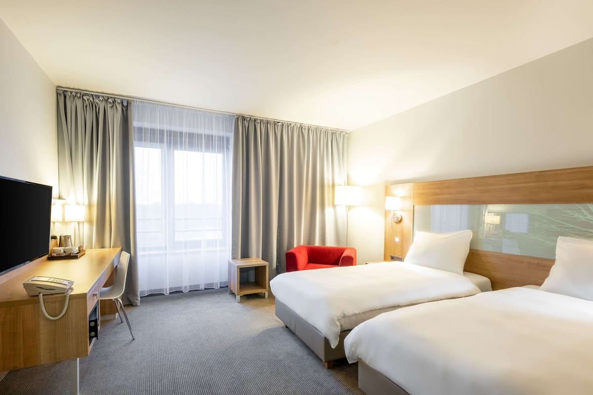 Ein Hotelzimmer mit zwei Betten, einem Schreibtisch mit Telefon, einem roten Sessel und einem Fernseher.