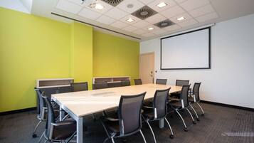 Una sala de conferencias con una larga mesa, sillas, una pantalla de proyector y una pizarra.