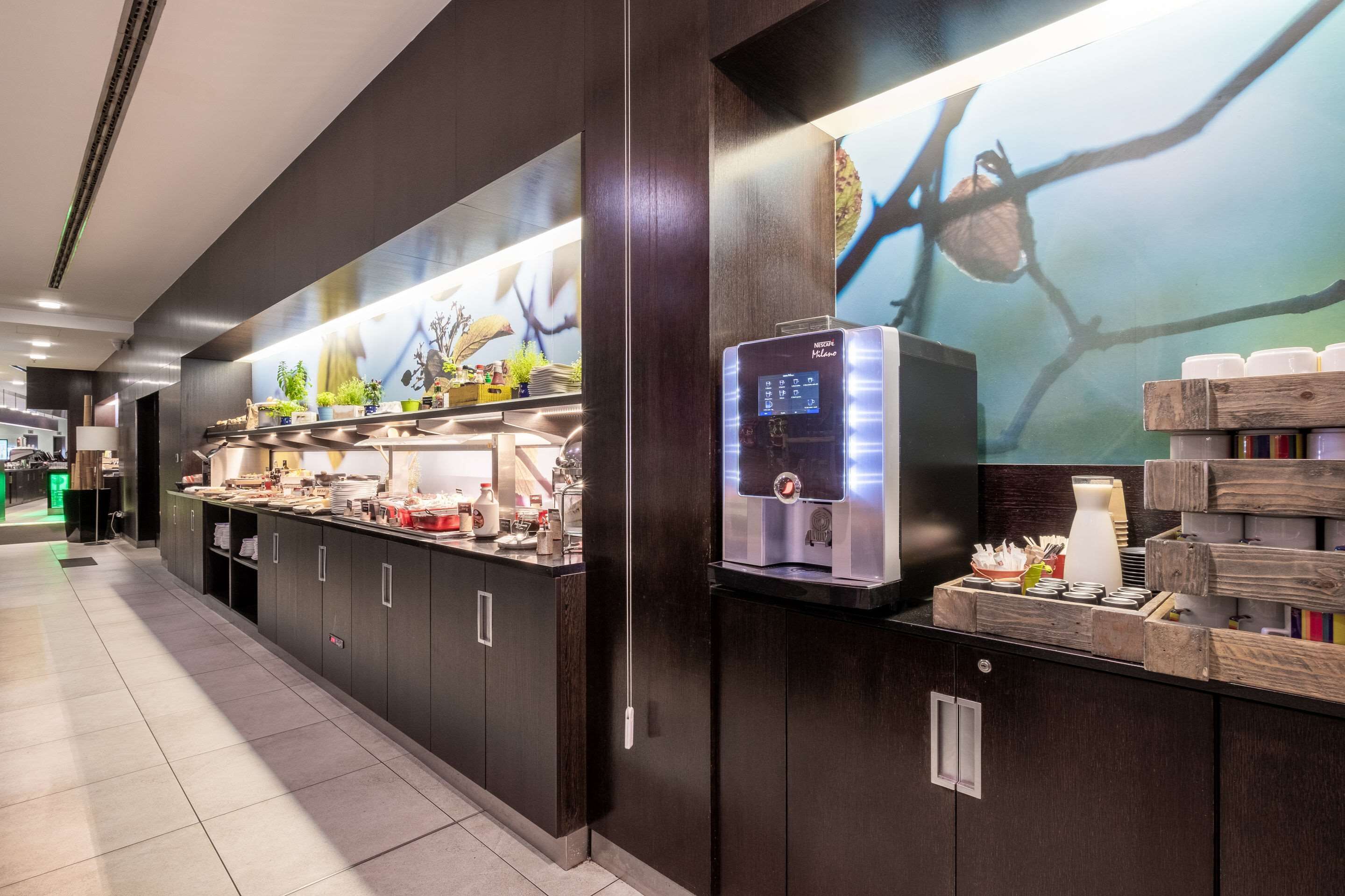 A modern kitchen area with a coffee machine, a counter with various food items, and a mural on the wall.
