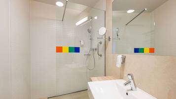 Un bany modern amb dutxa tancada amb vidre, un lavabo blanc amb aixeta cromada i un mirall sobre el lavabo.