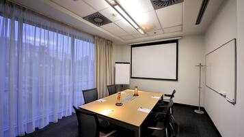 A conference room with a large table, chairs, a projector screen, and a whiteboard.