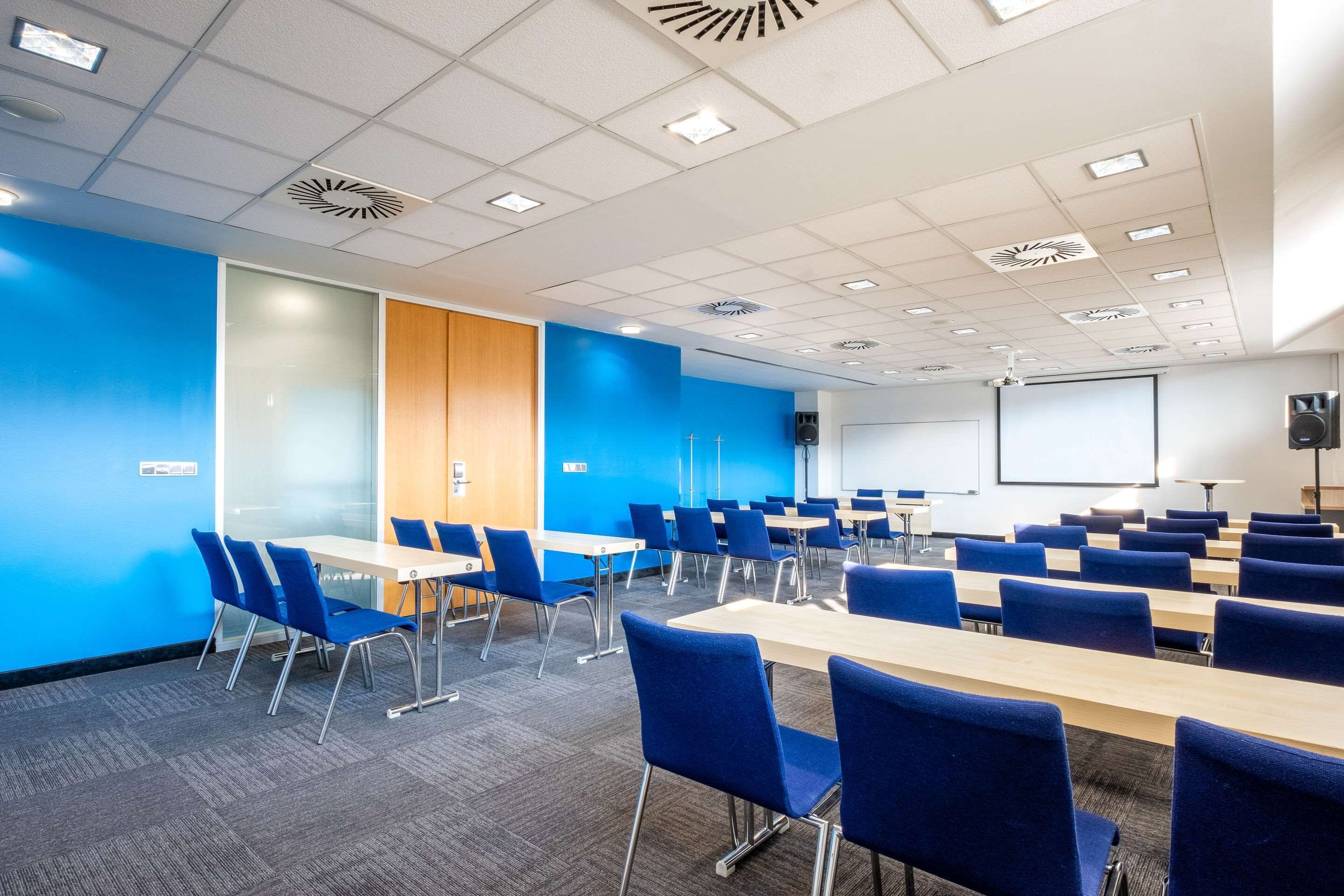 Un salón de conferencias con paredes azules, techo blanco y una pantalla para proyector.