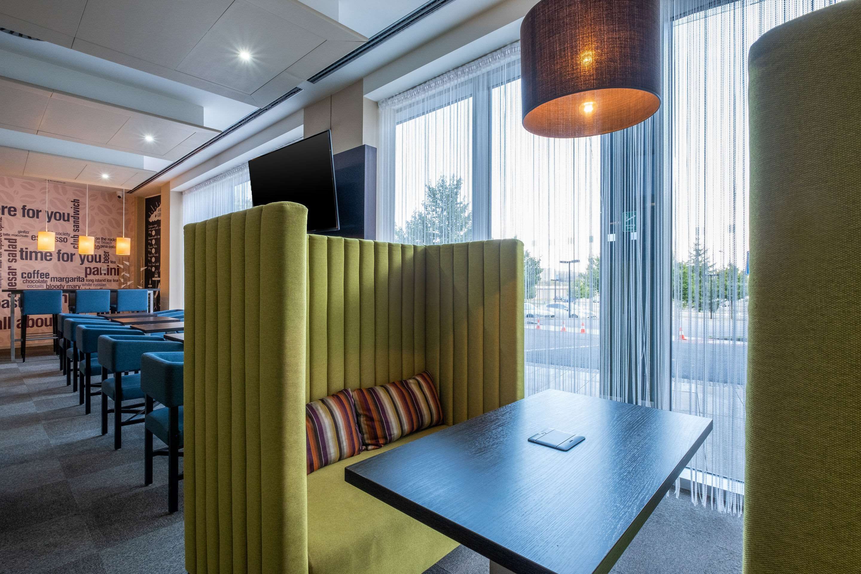 A modern hotel room with a seating area, a flat-screen TV, and large windows offering a view of the street.