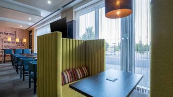A modern hotel room with a seating area, a flat-screen TV, and large windows offering a view of the street.