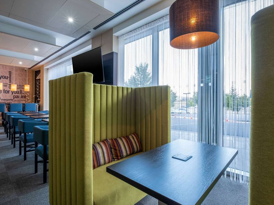 A modern hotel room with a seating area, a flat-screen TV, and large windows offering a view of the street.