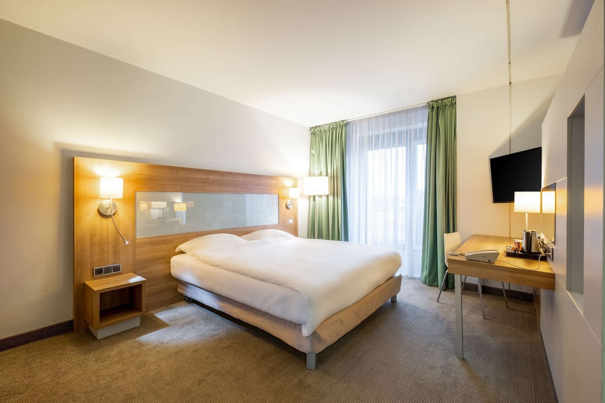 Ein Hotelzimmer mit Bett, Nachttisch, Lampe und Schreibtisch mit Stuhl.
