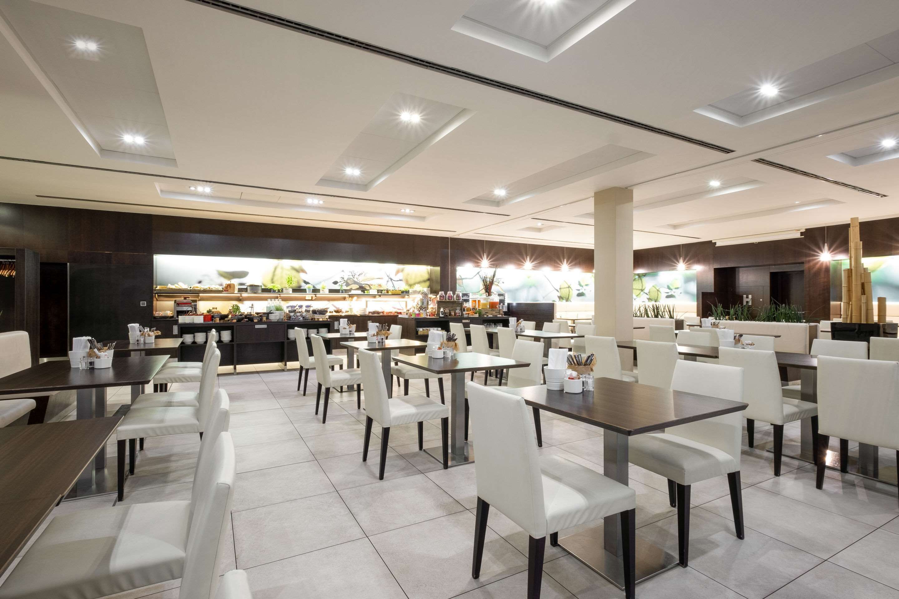 A modern restaurant with multiple dining tables and chairs, a bar area, and a kitchen in the background.