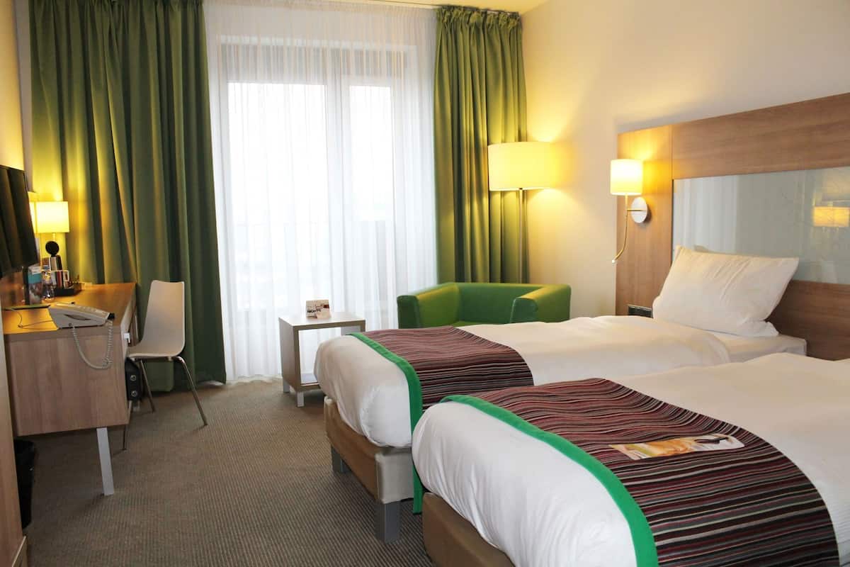 Ein Hotelzimmer mit zwei Betten, einem Schreibtisch mit Telefon, einem Sessel, einem kleinen Tisch und einer Lampe.