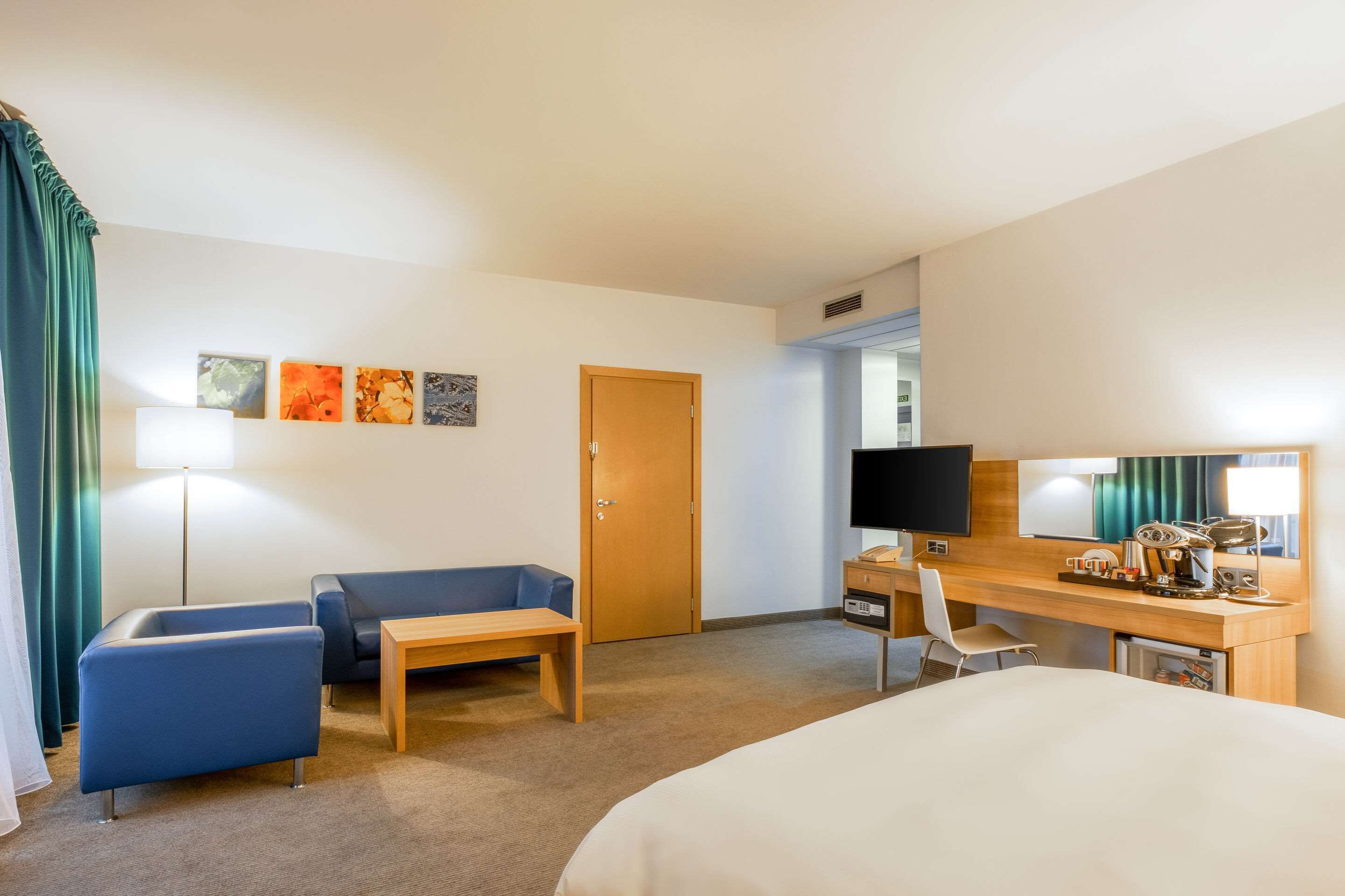 Une chambre d’hôtel comprenant un lit, un bureau avec un ordinateur, une chaise, un canapé, une lampe et des œuvres d’art accrochées au mur.