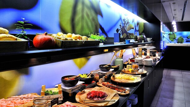 A buffet with various food items and a large illuminated wall in the background. - Quality Hotel Ostrava City (Ostrava)