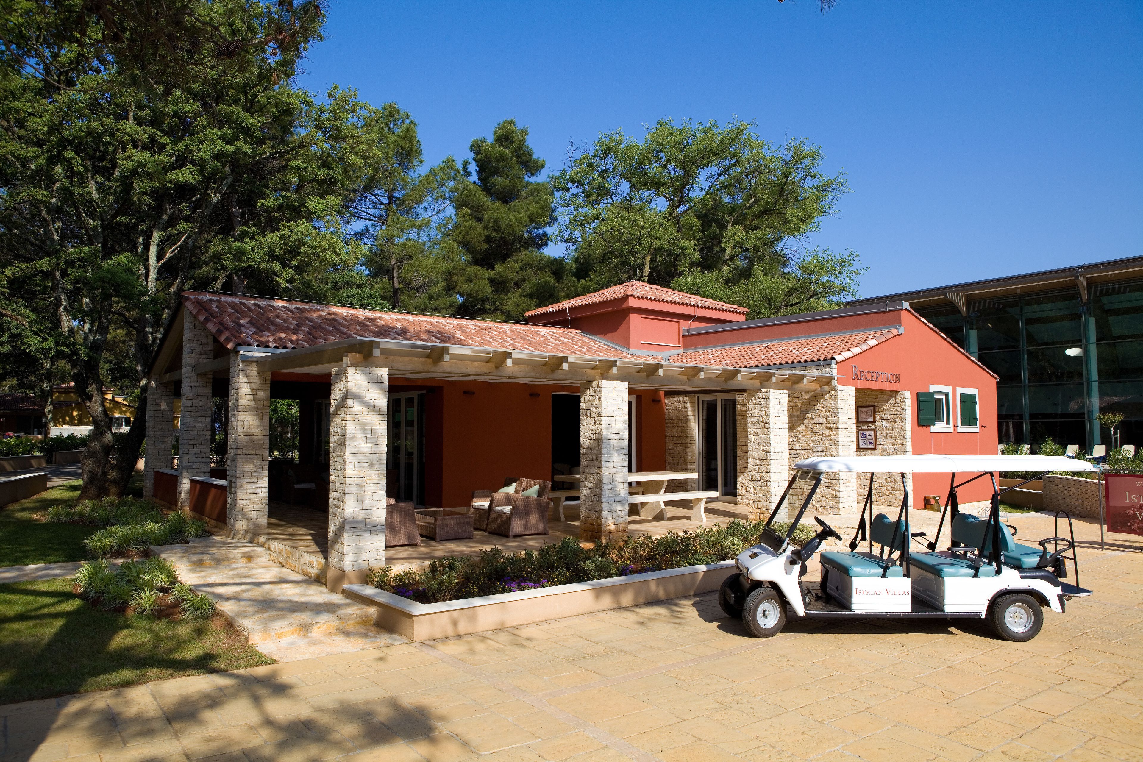 Un espace extérieur aménagé, abrité et doté de piliers en pierre, ainsi qu’une terrasse et un véhicule de golf stationné à proximité.