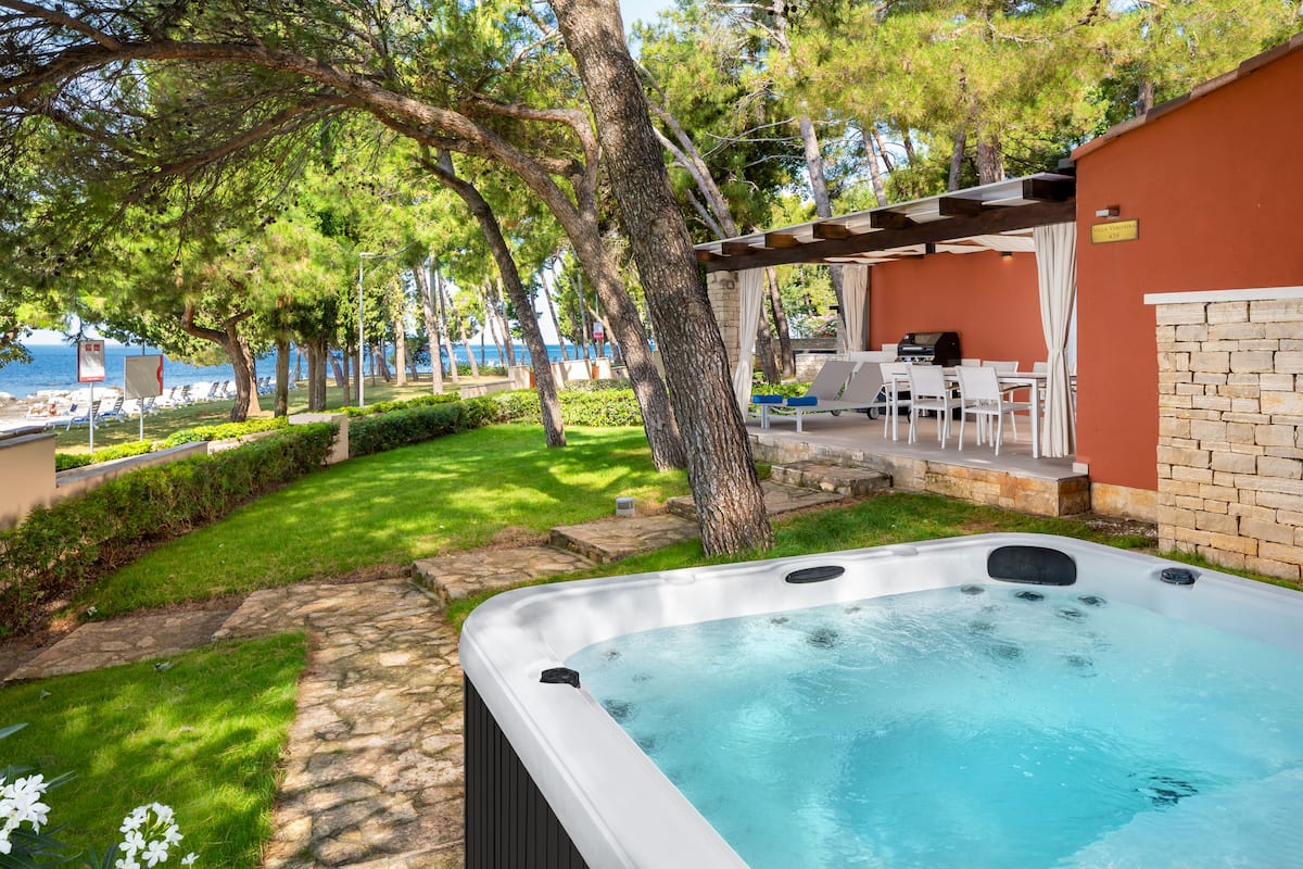A hot tub in a garden with a patio area, a view of the sea, and a stone wall.