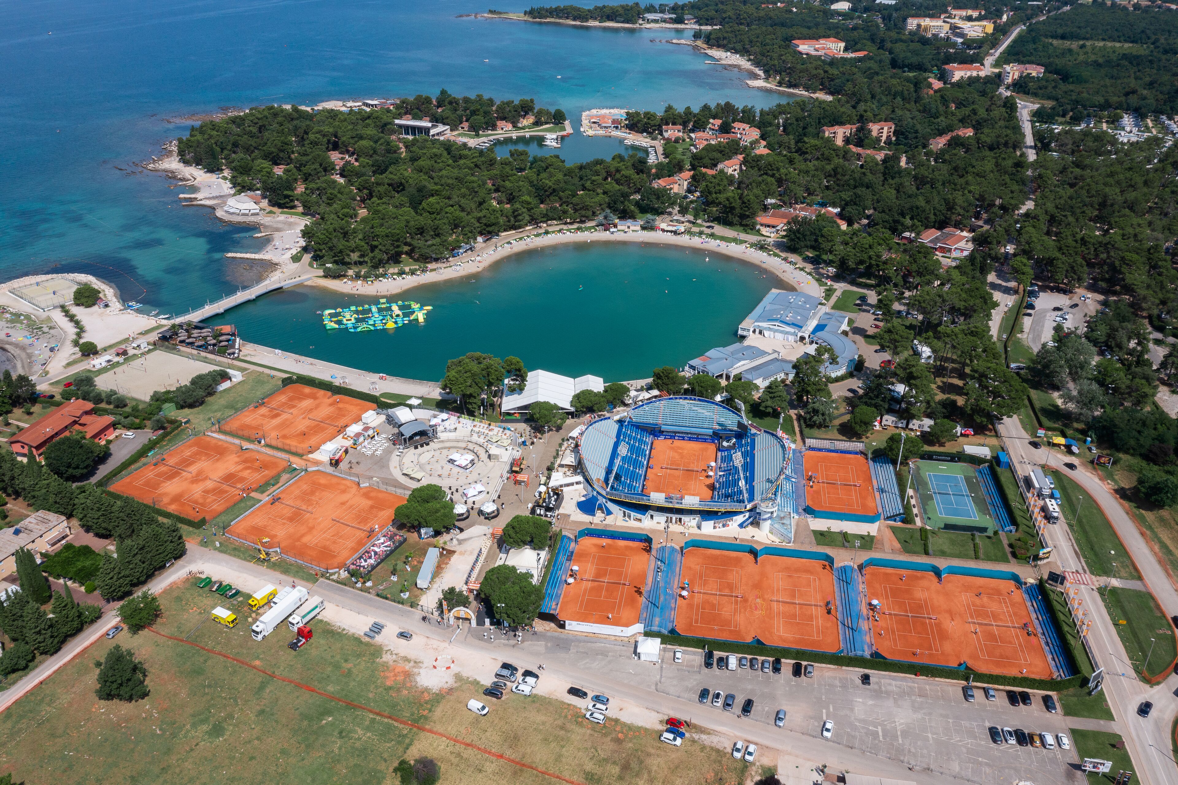 An aerial view of a coastal area with a tennis court complex, a beach, and surrounding residential buildings.