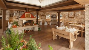 Een rustiek interieur met een stenen open haard, houten tafels en banken.