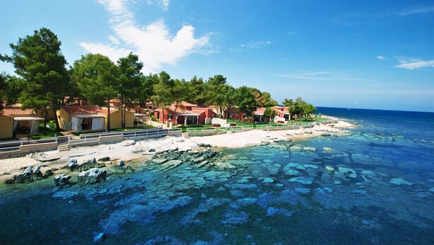 Een kusthotel met helderblauw water, een zandstrand en weelderige begroeiing.