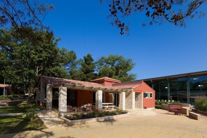 A red building with a tiled roof, stone pillars, and a covered patio area with outdoor seating.