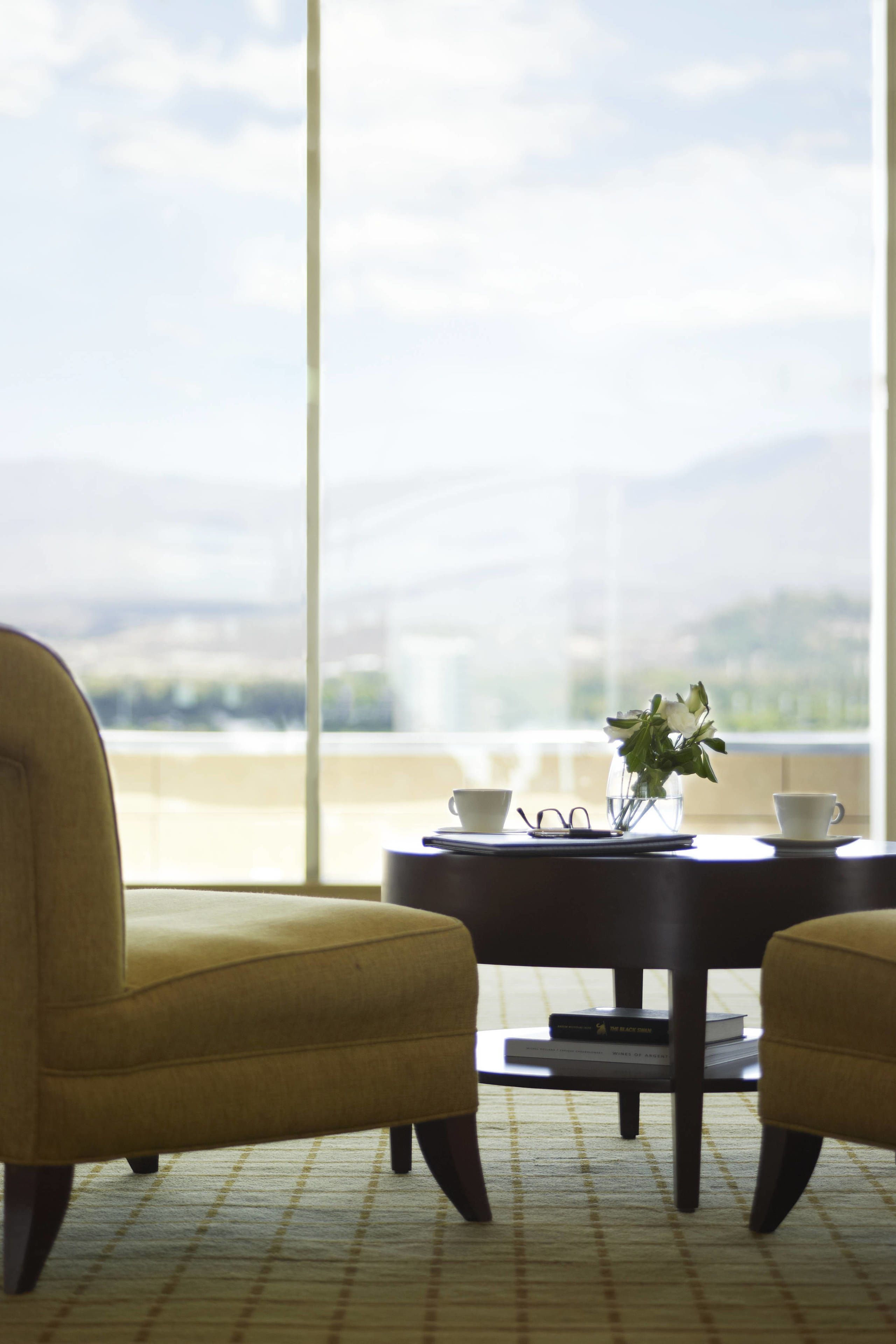 A room with a large window, a round table with two chairs, a vase with flowers, and a pair of glasses on the table.