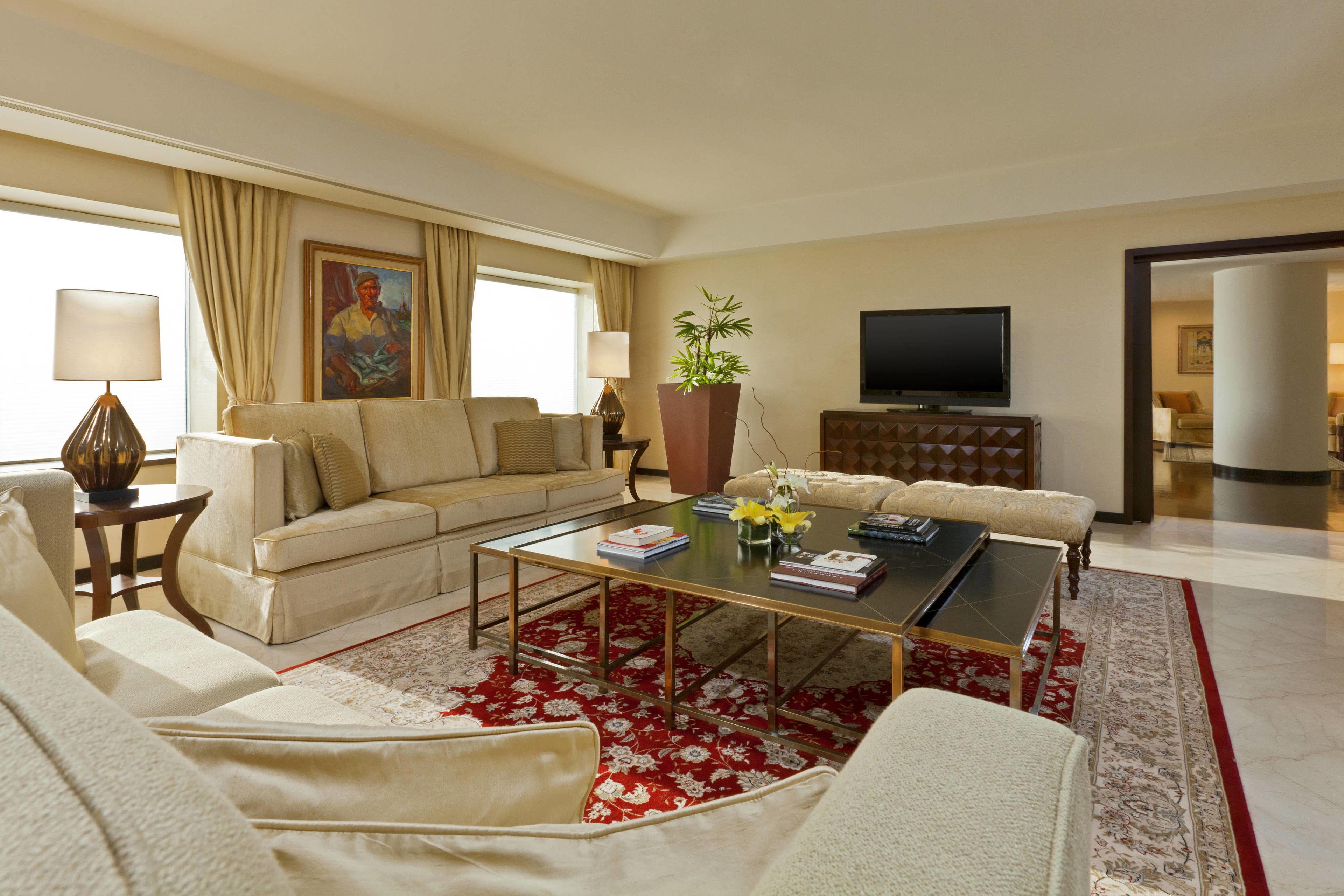 A modern living room with a sofa, armchairs, a coffee table, a television, and a large window with curtains.